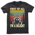 A dark gray t-shirt featuring a happy raccoon with a colorful striped background with tree silhouettes. The shirt features the quote "FIRST OF ALL, I'M A DELIGHT".