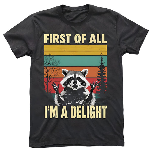 A dark gray t-shirt featuring a happy raccoon with a colorful striped background with tree silhouettes. The shirt features the quote "FIRST OF ALL, I'M A DELIGHT".