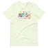 A light green t-shirt with a colorful autism awareness design. "Autism" is surrounded by colorful, childlike drawings with "accept understand love" underneath.