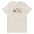 A sand t-shirt with a colorful autism awareness design. "Autism" is surrounded by colorful, childlike drawings with "accept understand love" underneath.