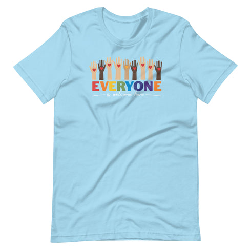 A light blue t-shirt with a colorful "Everyone is welcome here" design. Above the phrase, multicultural hands are shown with hearts on them.