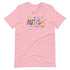 A pink t-shirt with a colorful autism awareness design. "Autism" is surrounded by colorful, childlike drawings with "accept understand love" underneath.