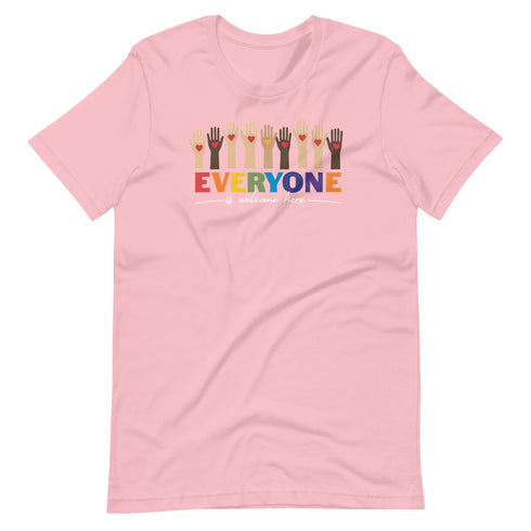 A pink t-shirt with a colorful "Everyone is welcome here" design. Above the phrase, multicultural hands are shown with hearts on them.