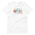 A white t-shirt with a colorful autism awareness design. "Autism" is surrounded by colorful, childlike drawings with "accept understand love" underneath.